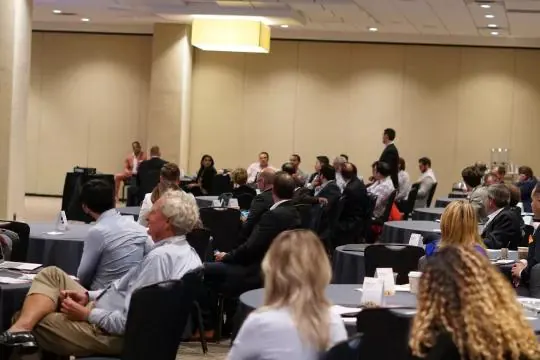 Delegates seated at round tables during a TechNext presentation